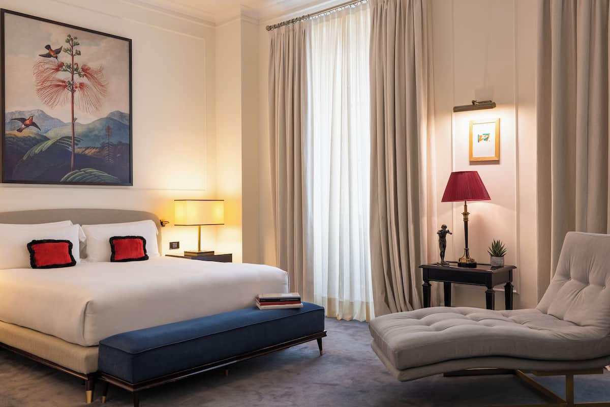 A hotel room with a large bed, a bedside table with a lamp, a chair, and a painting on the wall.