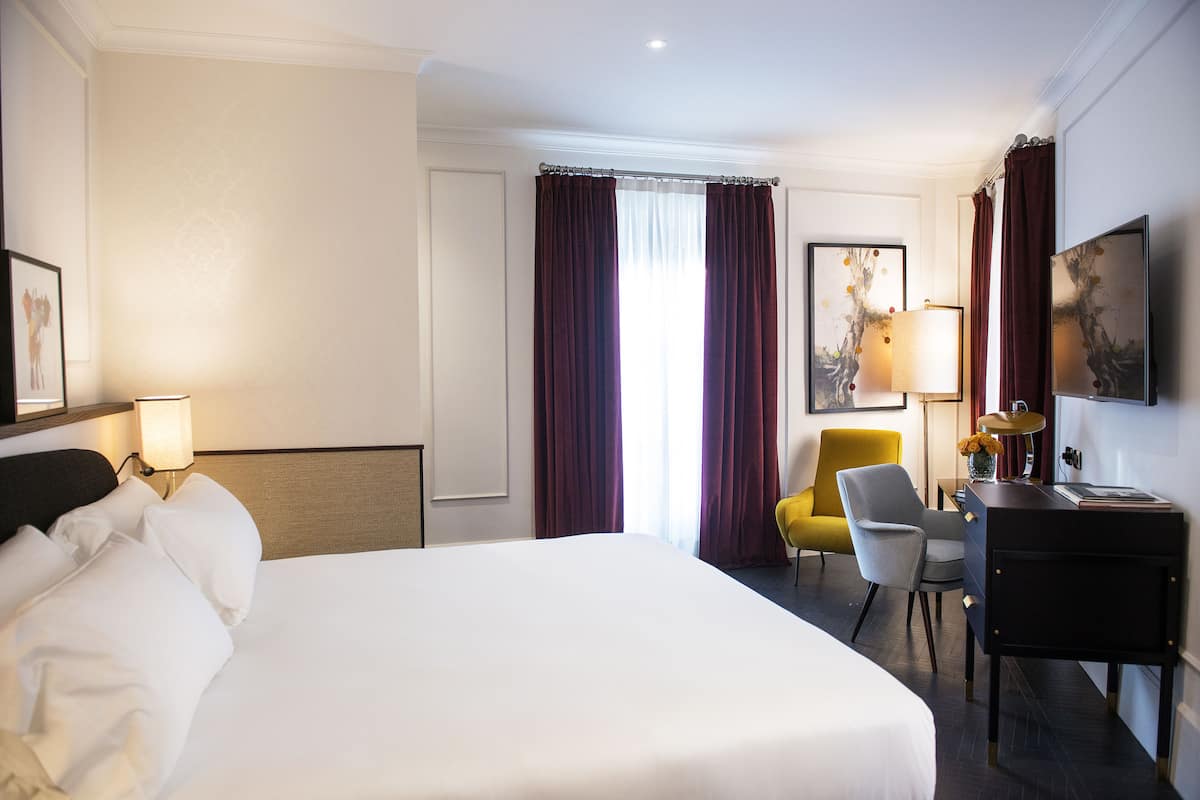 A hotel room with a large bed, a desk, a chair, and a lamp.