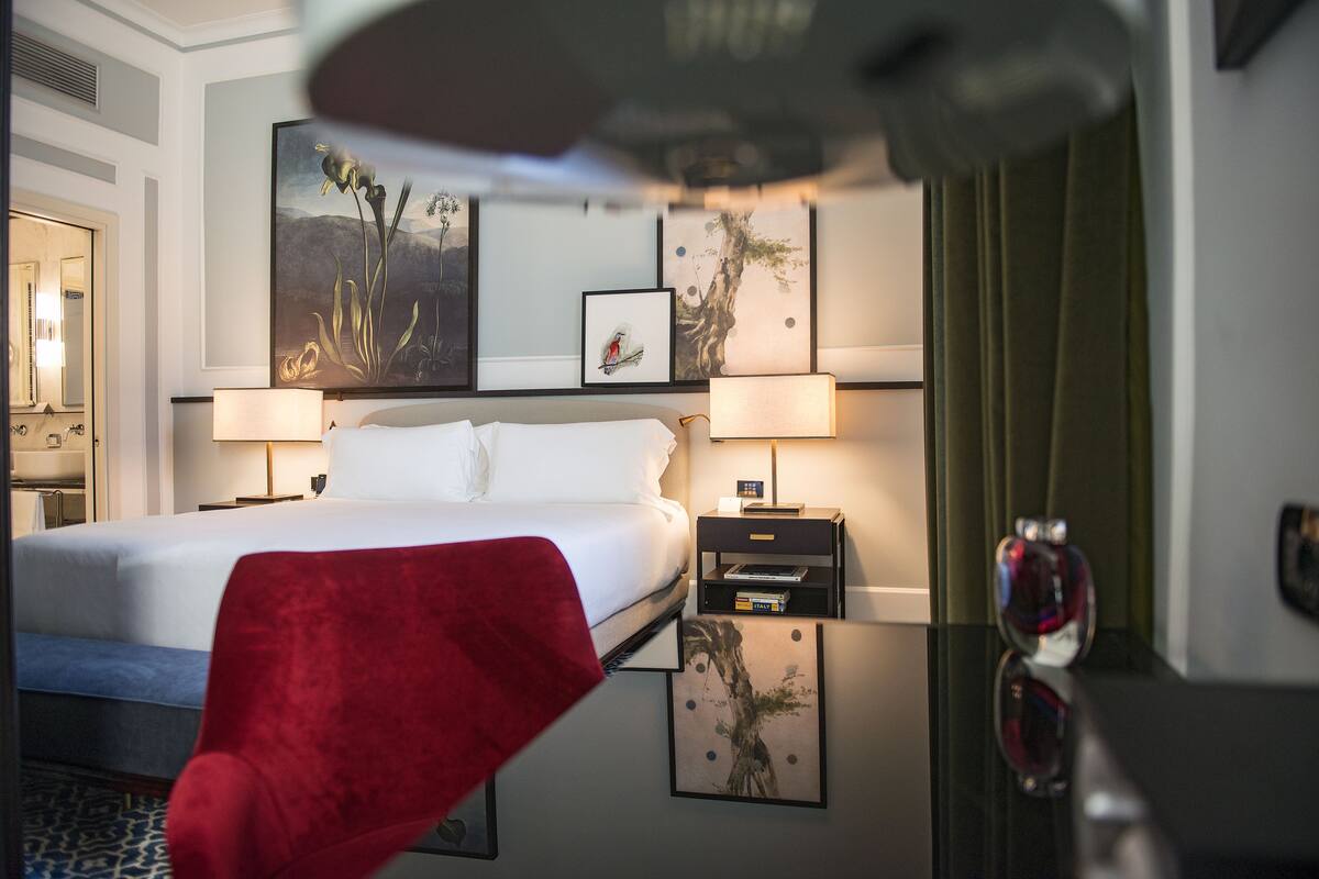 A hotel room with a bed, two bedside tables, a red chair, and artwork on the walls.