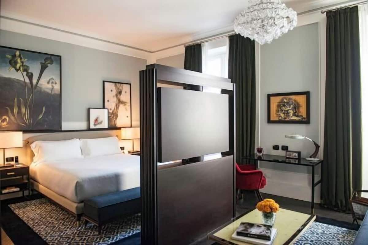 A hotel room with a bed, a desk, a chair, a coffee table, and artwork on the walls.