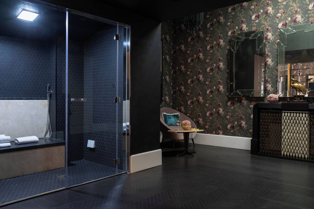 A modern bathroom with a glass shower enclosure, a vanity with a mirror, and a floral wallpaper design.