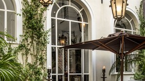 An outdoor dining area with tables set for two, surrounded by white walls and arched windows. - Hotel Vilòn (Rome)