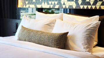 A neatly made bed with white and patterned pillows, a dark headboard, and a geometric-patterned wall behind it.