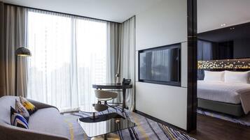 Moderni hotellihuone, jossa on sohva, ruokapöytä, televisio ja sänky.