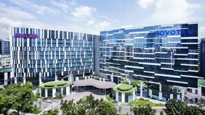 Un hotel moderno con fachada de vidrio, que incluye las marcas Mercure y Novotel, y presenta un patio central con jardines.