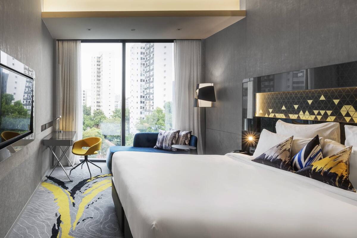 Une chambre d’hôtel moderne, dotée d’un grand lit, d’un bureau, d’une chaise et offrant une vue sur de hauts immeubles.