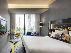 Een moderne hotelkamer met een groot bed, een bureau, een stoel en uitzicht op hoge gebouwen.