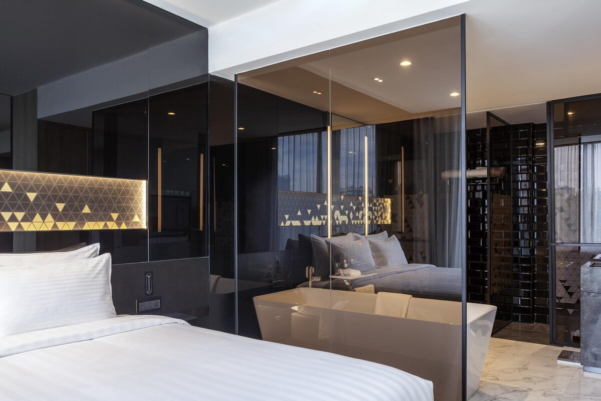 Ein modernes Hotelzimmer mit einem großen Bett, einer Sitzecke und einer Glasabtrennung.