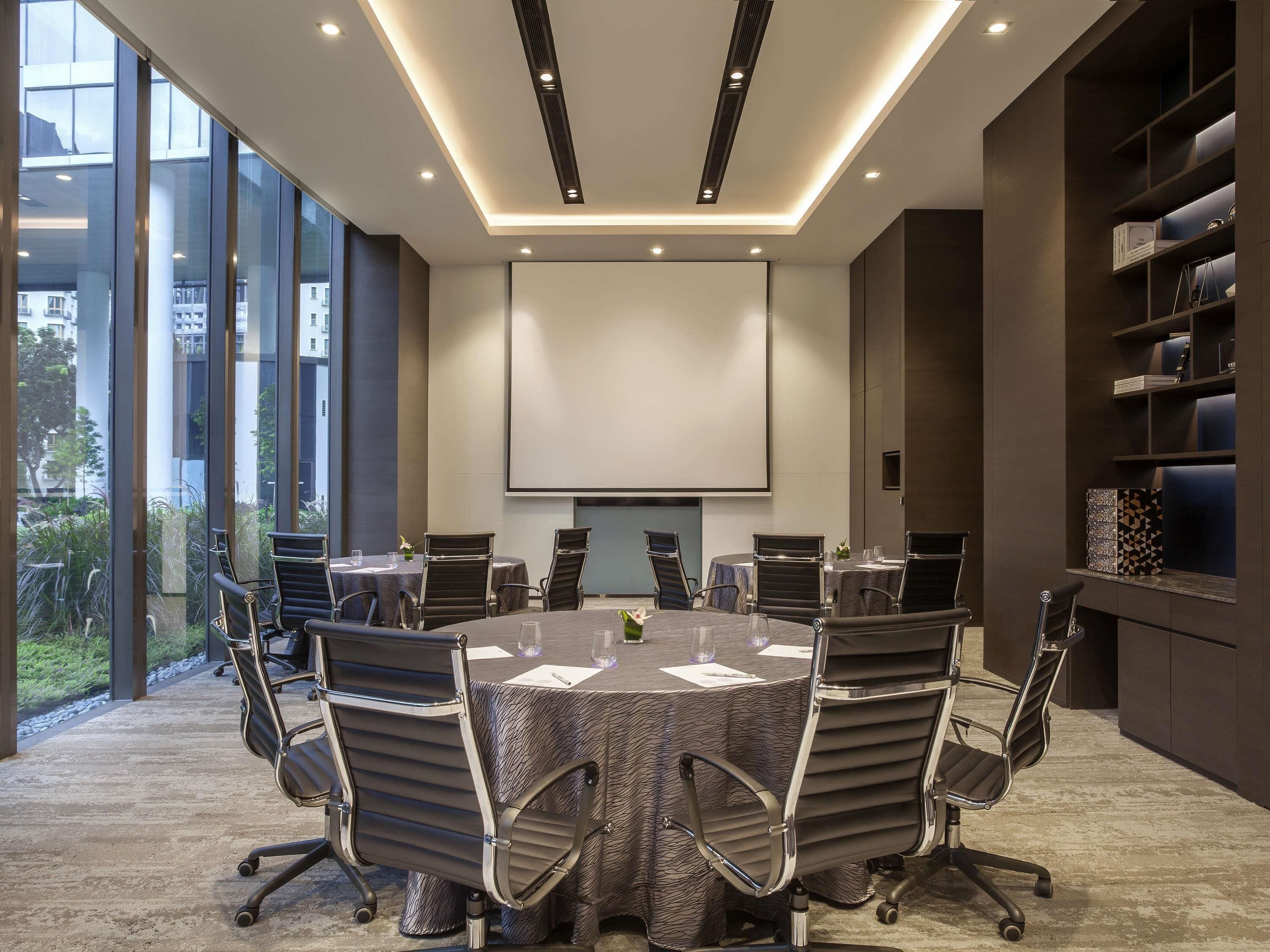 A conference room with a large table, chairs, a projector screen, and a bookshelf.