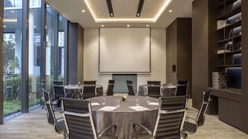 A conference room with a large table, chairs, a projector screen, and a bookshelf.