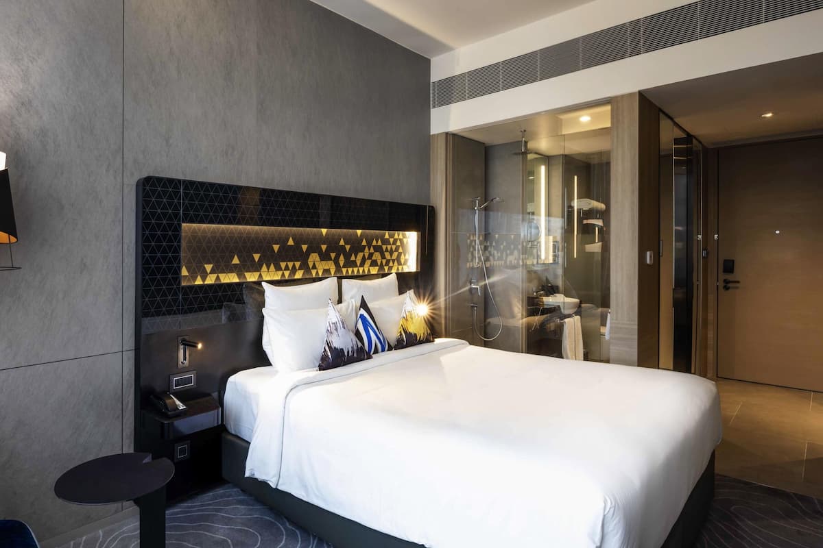 Une chambre d’hôtel moderne avec un grand lit, une table de chevet et une douche séparée par une paroi de verre.