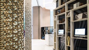 Un interior moderno con un muro de patrón geométrico, una recepción de mármol y estanterías con objetos decorativos y monitores.