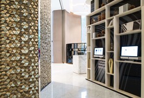A modern interior with a geometric patterned wall, a marble reception desk, and shelves with decorative items and monitors.