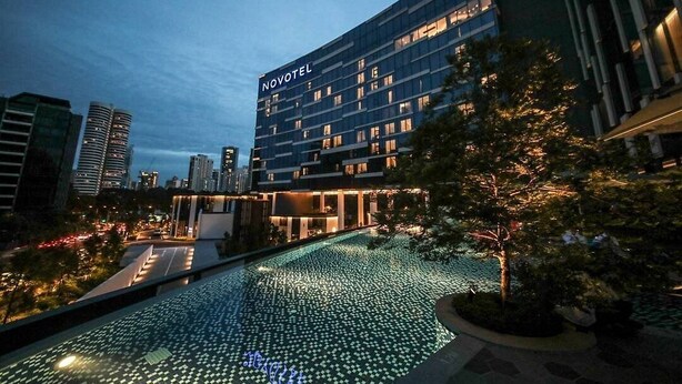 Un hotel Novotel con diseño moderno, que cuenta con una piscina en la azotea con baldosas iluminadas.