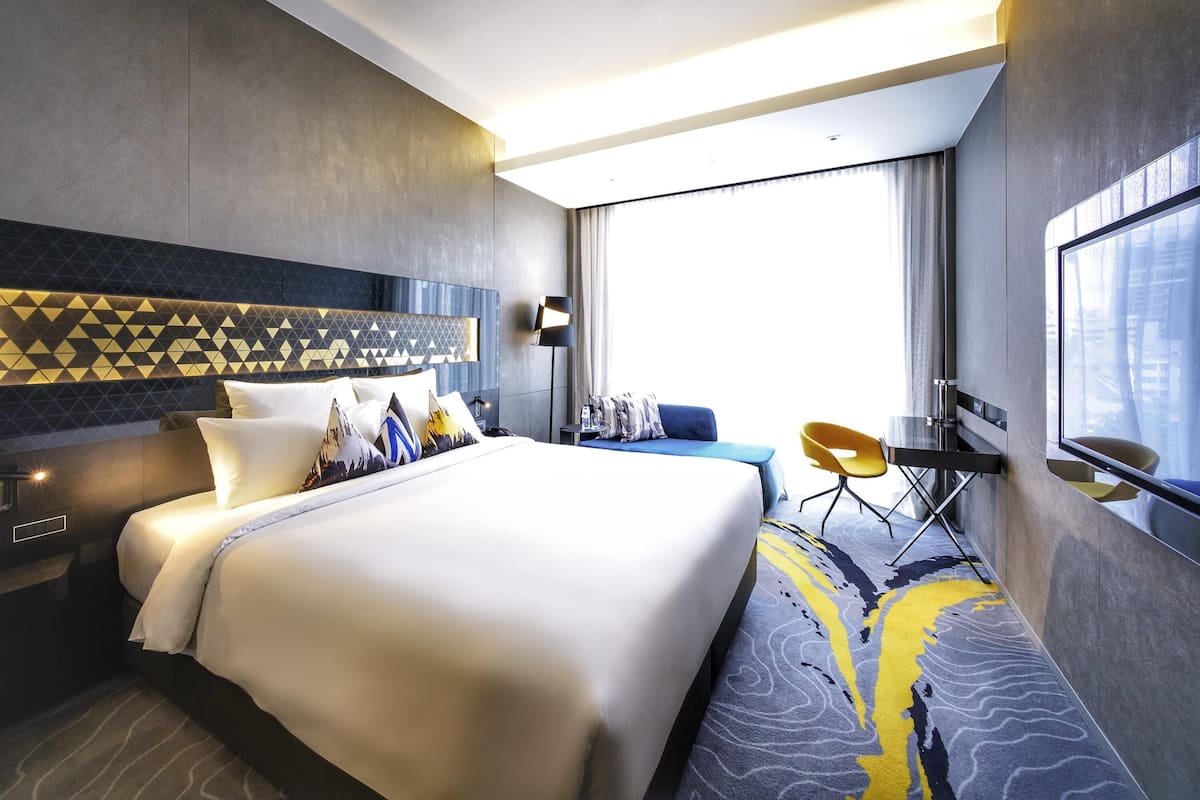 Une chambre d’hôtel moderne avec un grand lit, un bureau, une chaise et une grande fenêtre.
