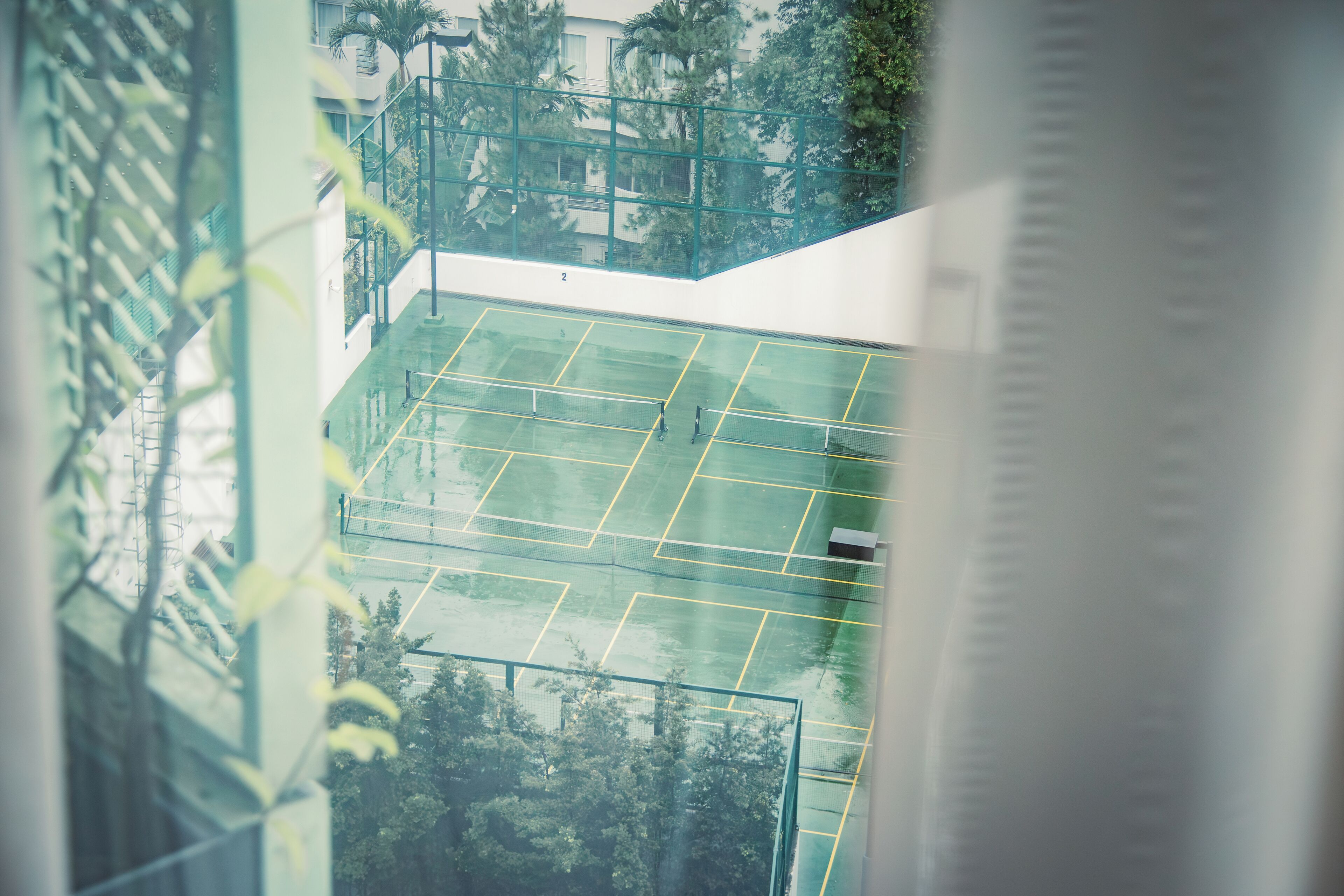 Una cancha de tenis con red, rodeada de vegetación y un edificio con balcón.