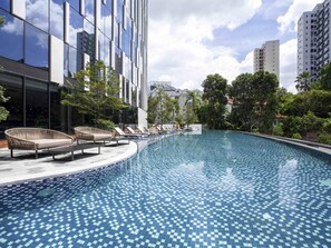 Een modern hotel met een zwembad, ligbedden en uitzicht op omliggende gebouwen.