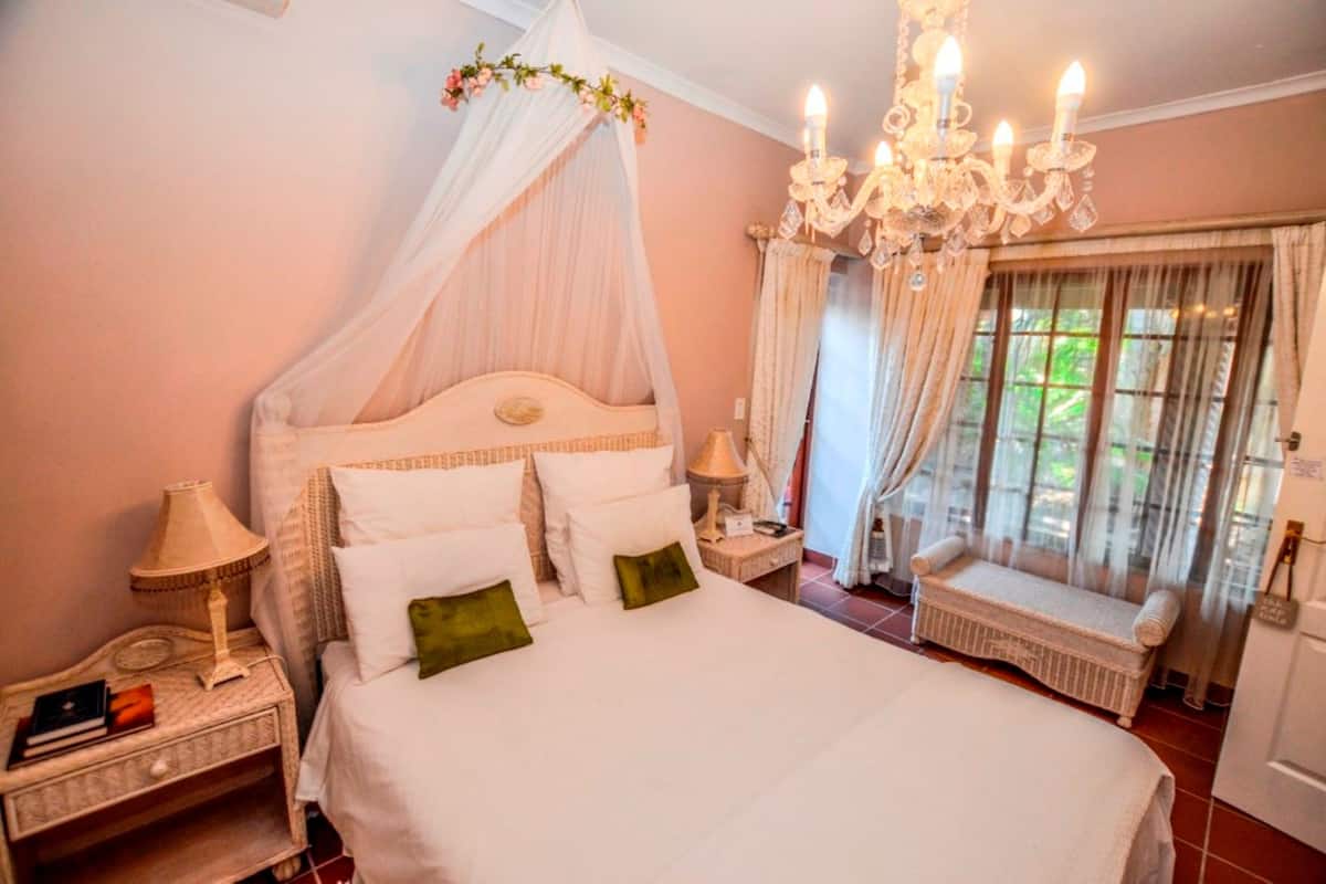 A bedroom with a four-poster bed, a chandelier, a nightstand, and a window with curtains.