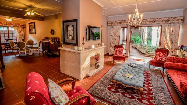 A spacious living room with a fireplace, red upholstered sofas, a coffee table, and a large window offering a view of the outdoors. - Lavender House (Mbombela)