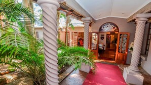 A hotel lobby with a red carpet, columns, and tropical plants. - Lavender House (Mbombela)