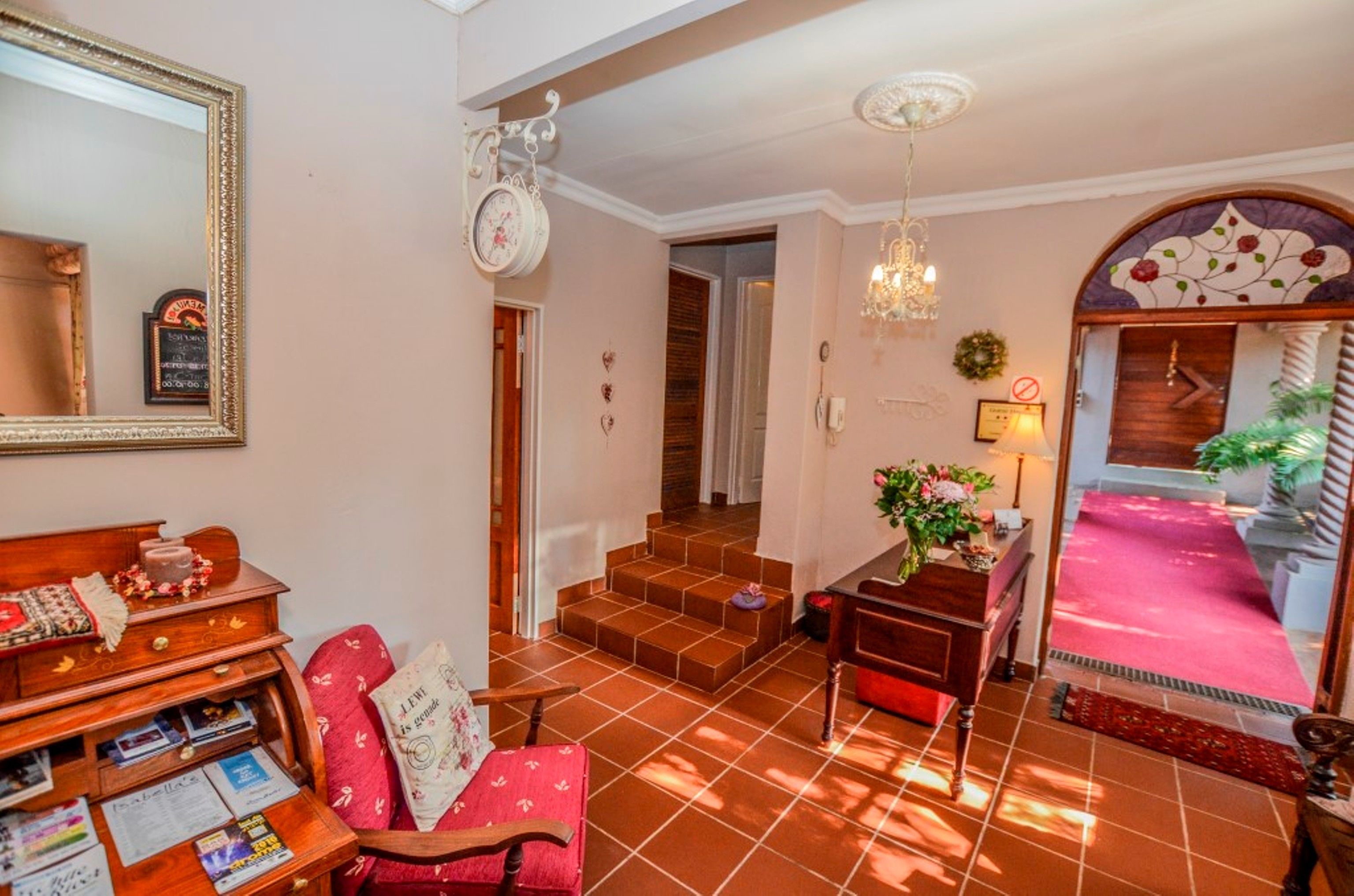 Una sala acogedora con chimenea, un sillón rojo, una mesita de madera y una escalera que lleva a un pasillo.