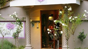 A hotel entrance with a brick pathway leading to a door, surrounded by greenery and a signboard. - Lavender House (Mbombela)
