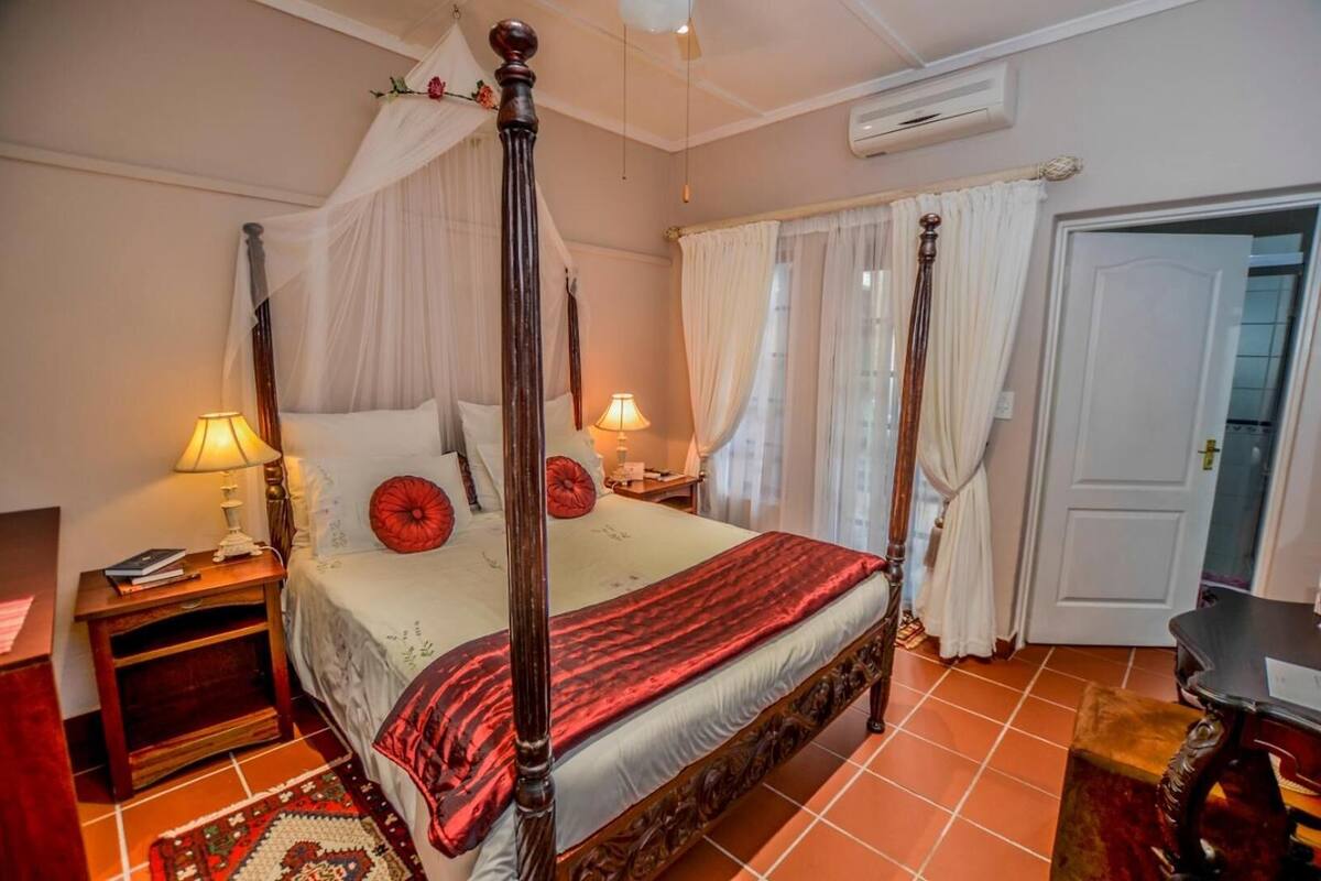 A four-poster bed with a canopy, a bedside table with a lamp, and a door to the right.