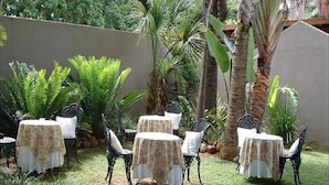 A patio area with tables and chairs, surrounded by lush greenery and palm trees. - Lavender House (Mbombela)