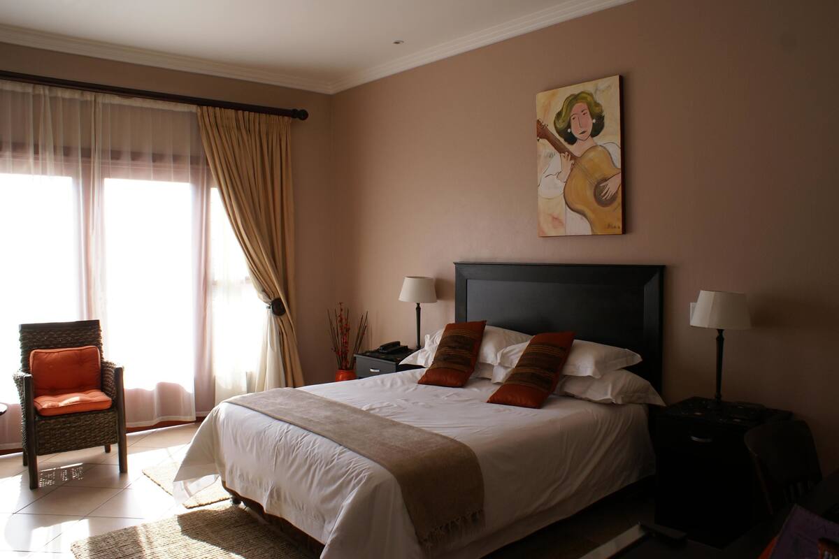 Een hotelkamer met een groot bed, een stoel, een nachtkastje en een schilderij aan de muur.
