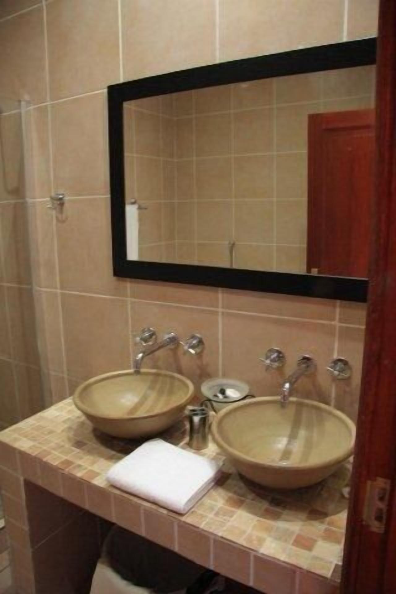 Um banheiro com duas pias bege, um espelho e uma toalha no balcão.