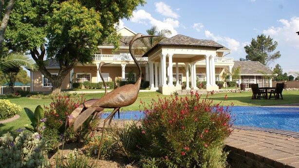 A large house with a pool, surrounded by a garden with a sculpture.