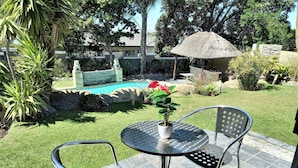 A patio area with a table and chairs, a small potted plant, and a pool in the background. - Mandalay Beach B & B (Cape Town)