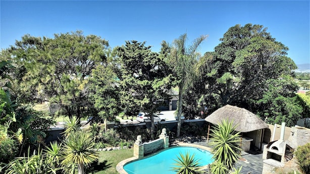 A swimming pool surrounded by tropical plants and a thatched-roof structure. - Mandalay Beach B & B (Cape Town)