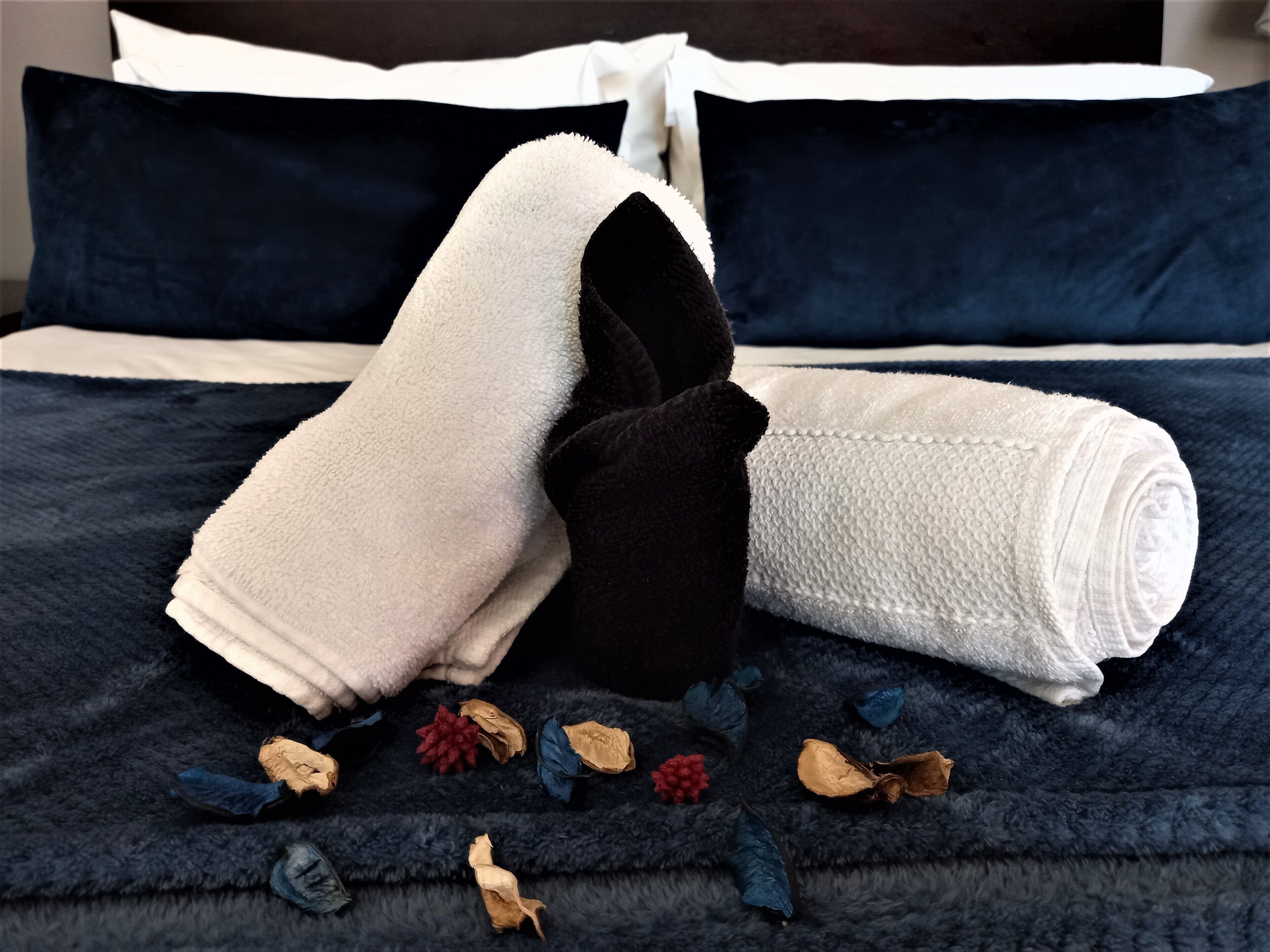 A neatly made bed with a dark blue bedspread, white and black towels, and dried flowers scattered on the bed.