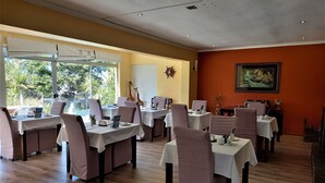 A restaurant with multiple tables and chairs, large windows with blinds, a whiteboard, and a framed picture on the wall. - Mandalay Beach B & B (Cape Town)