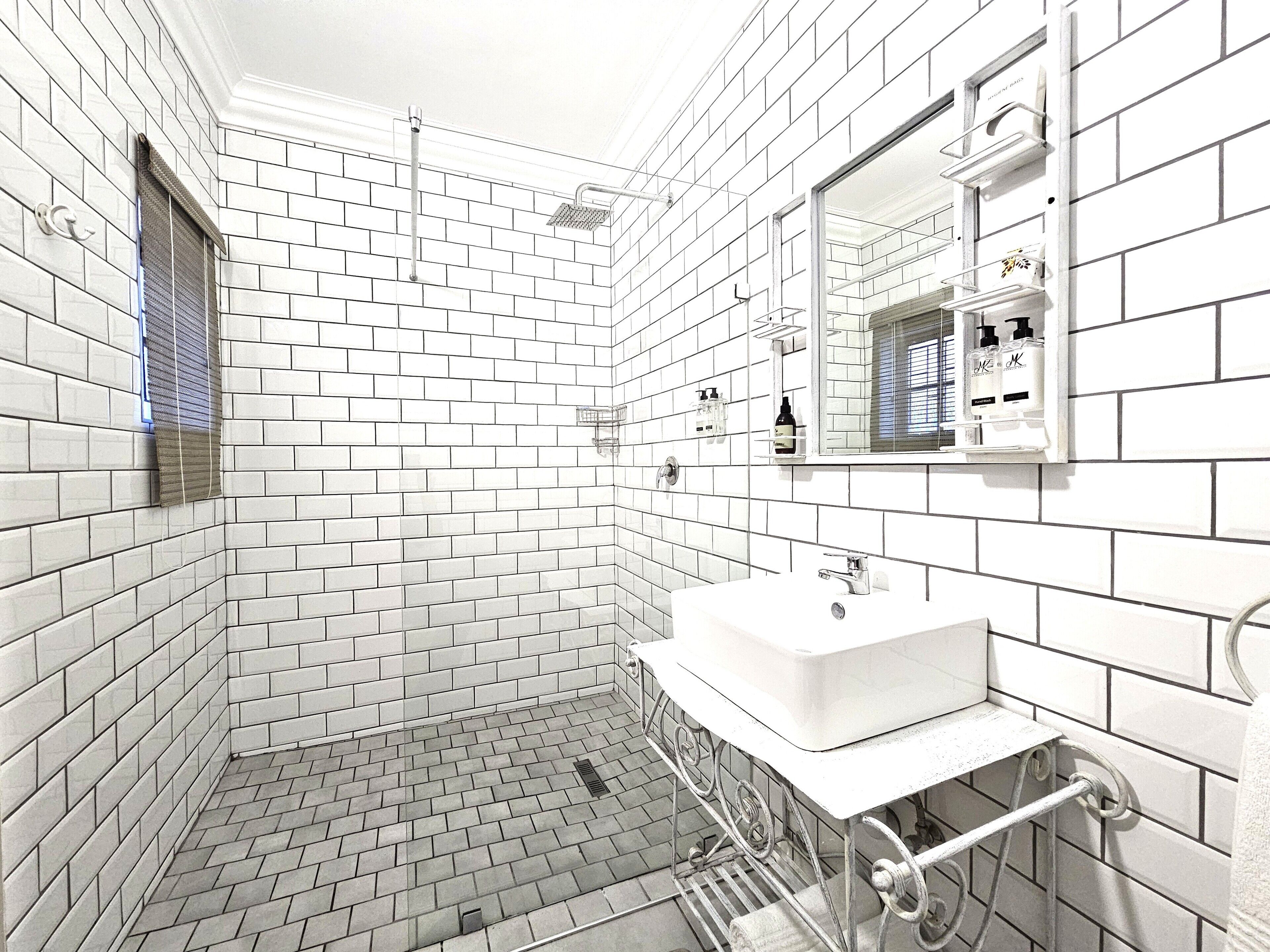 Un baño con azulejos blancos tipo metro, un lavamanos blanco y un espejo encima.
