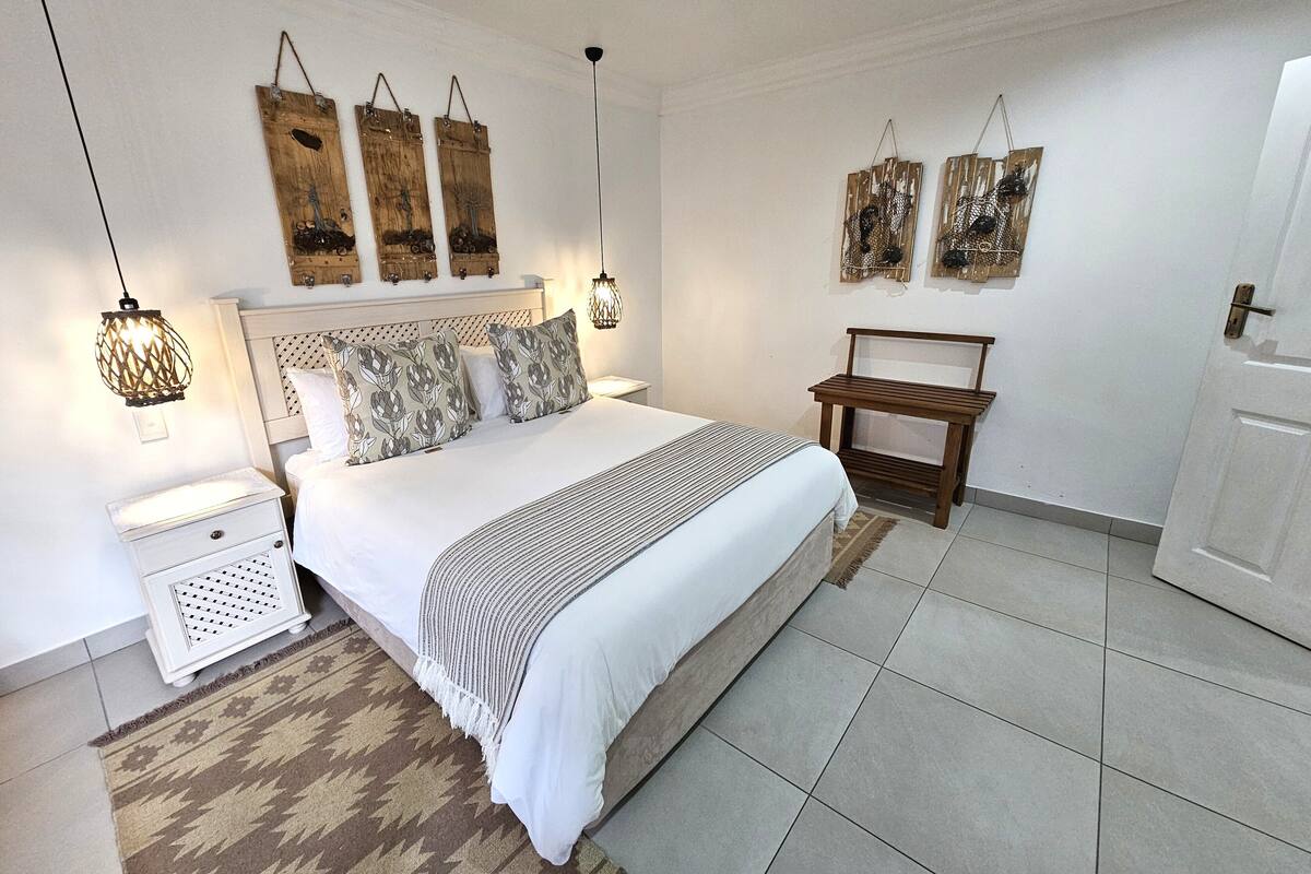 A bedroom with a large bed, two bedside tables, a nightstand, a wooden bench, and wall art.