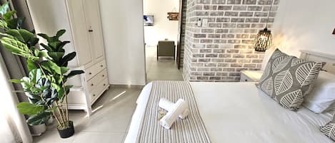 Un dormitorio moderno con una cama, una planta en maceta, un armario y una pared de ladrillo.
