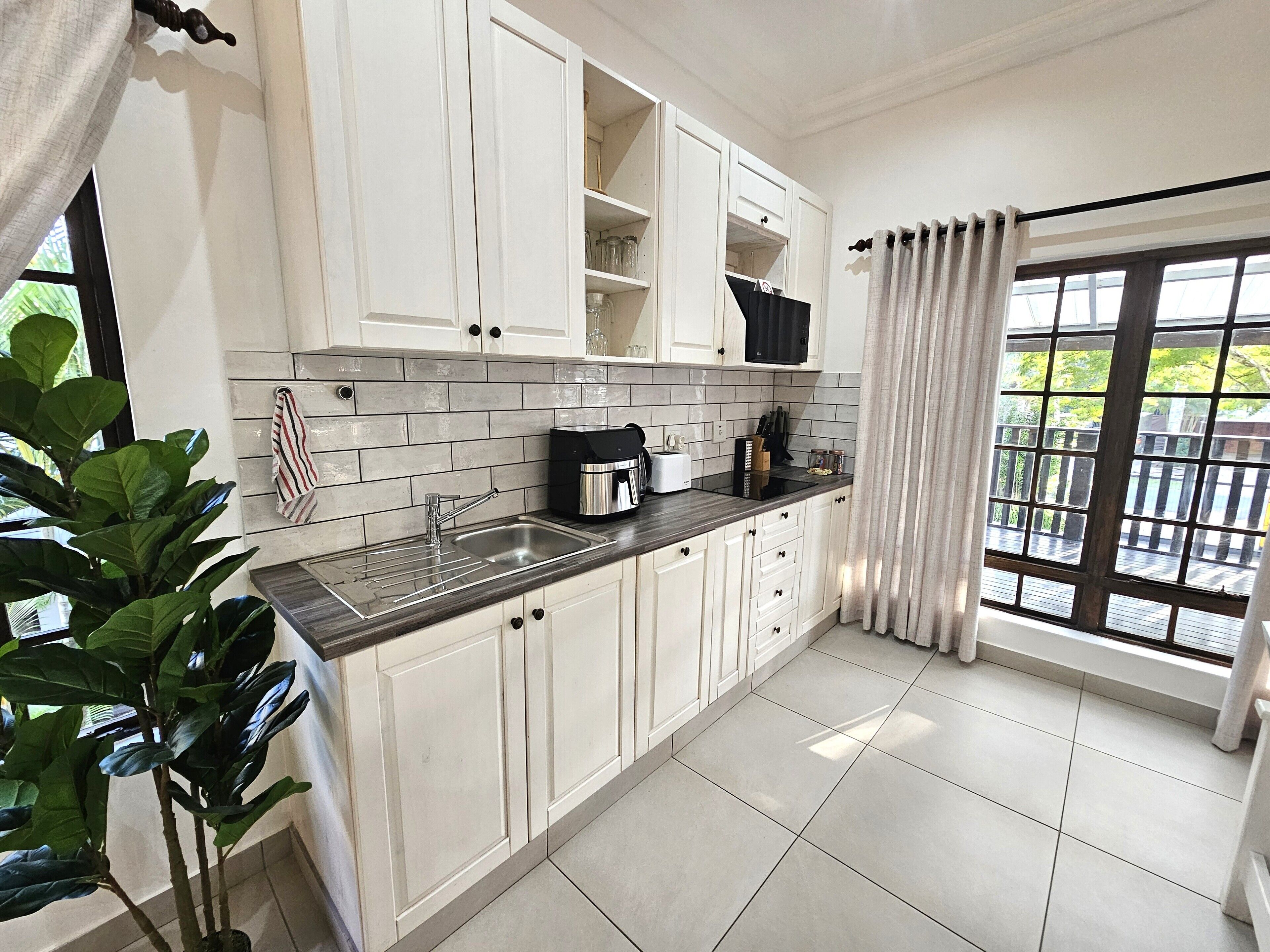 A modern kitchen with white cabinets, a black countertop, and a sink. There is a window with a view of greenery outside.