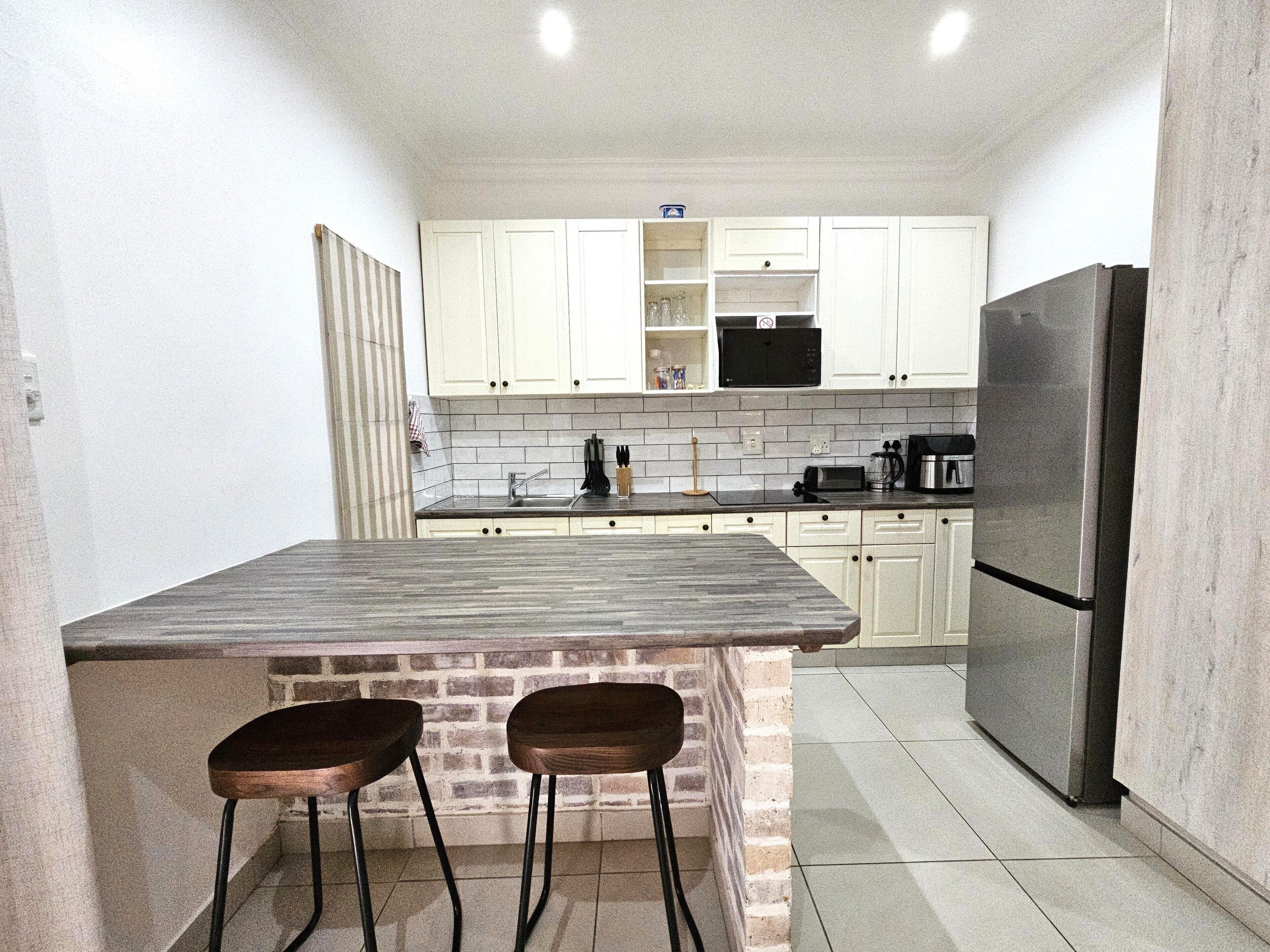 A kitchen with white cabinets, a black microwave, a stainless steel refrigerator, and two wooden stools.