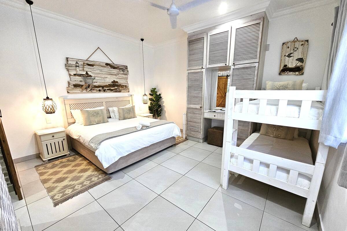 A bedroom with a bed, a nightstand, a bedside table, a hanging light fixture, a ceiling fan, and a bunk bed.