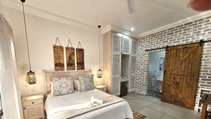 A bedroom with a large bed, bedside tables, a wardrobe, and a brick wall. - Leopard Tree Lodge (St. Lucia)