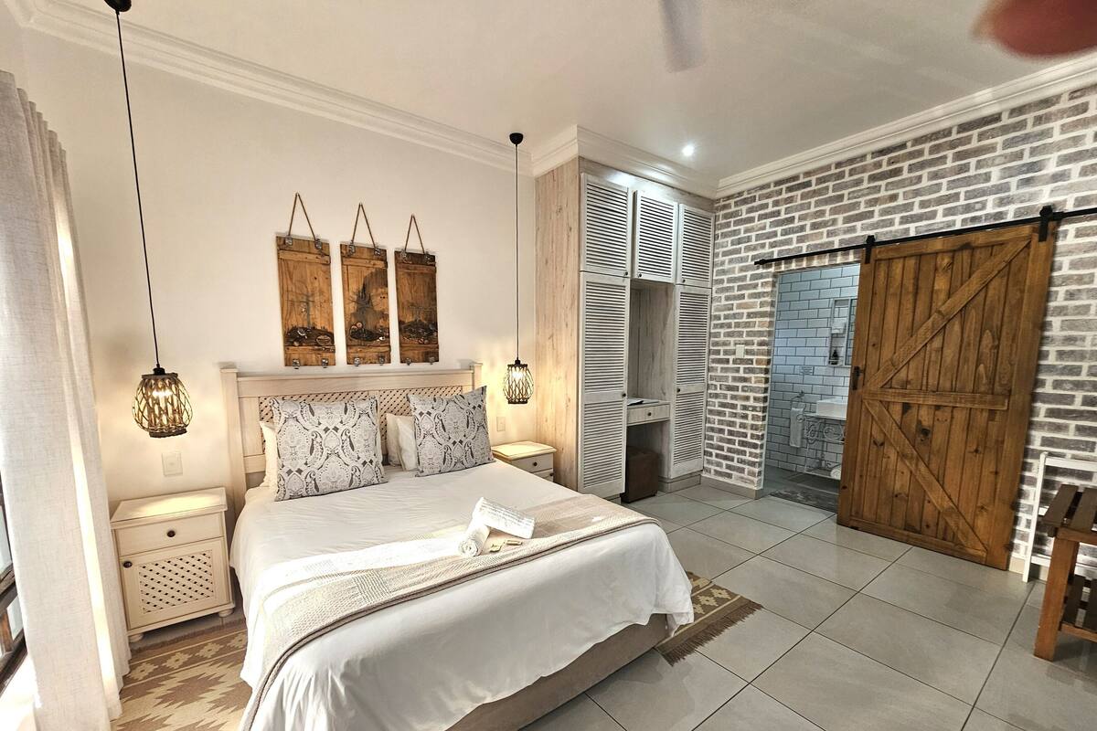 A bedroom with a large bed, bedside tables, a wardrobe, and a brick wall.