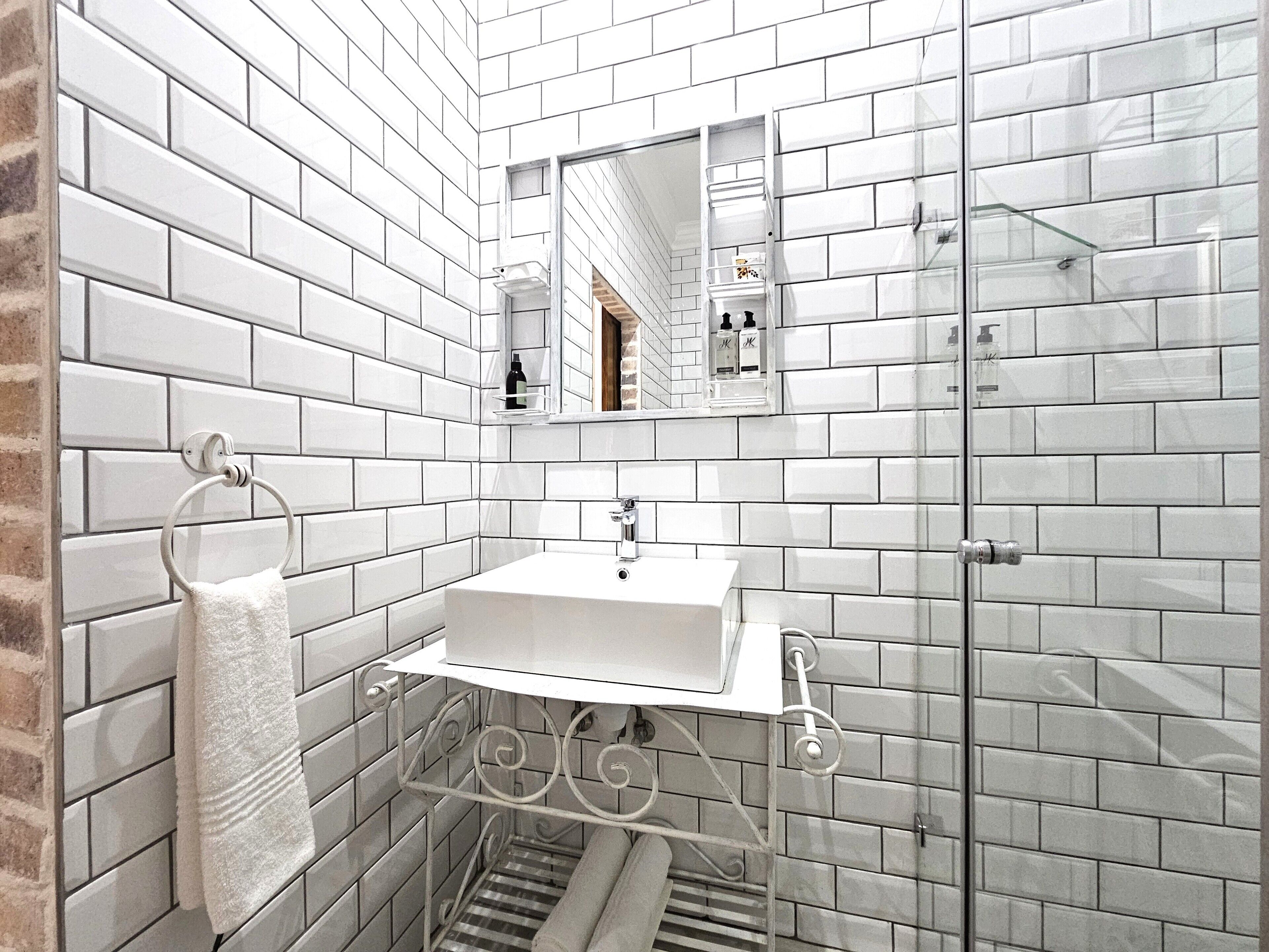 Une salle de bain avec des carreaux de métro blancs, un lavabo blanc, un porte-serviettes, un miroir et une paroi de douche en verre.