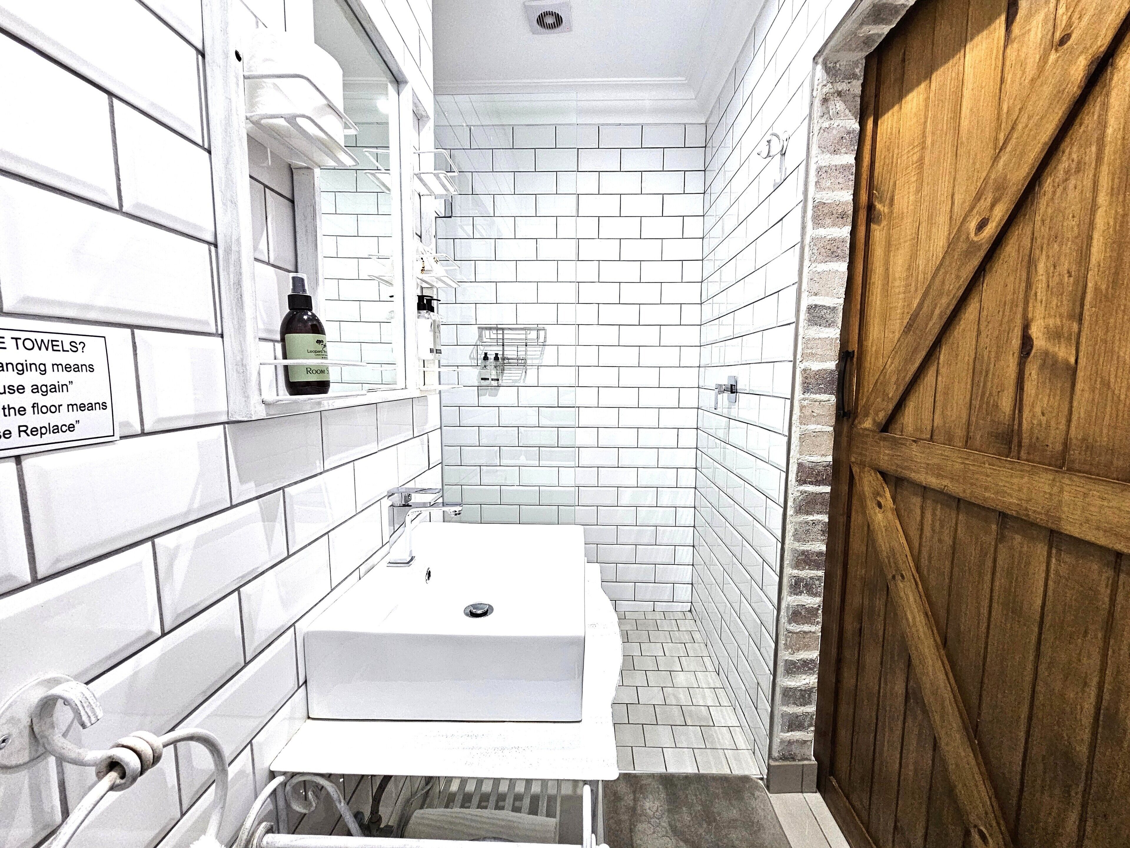 A narrow bathroom with white tiled walls, a white sink, and a wooden door.