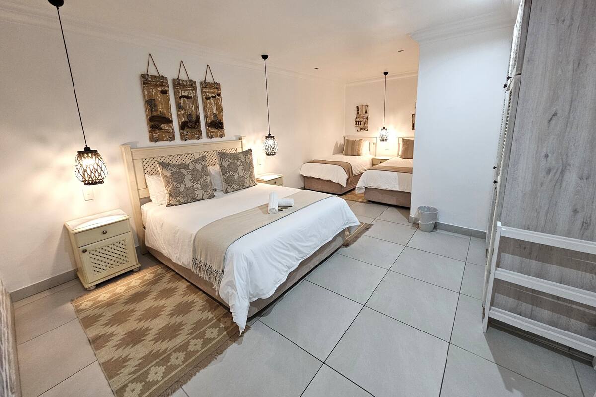 A bedroom with two beds, a nightstand, a lamp, and a wall-mounted shelf.