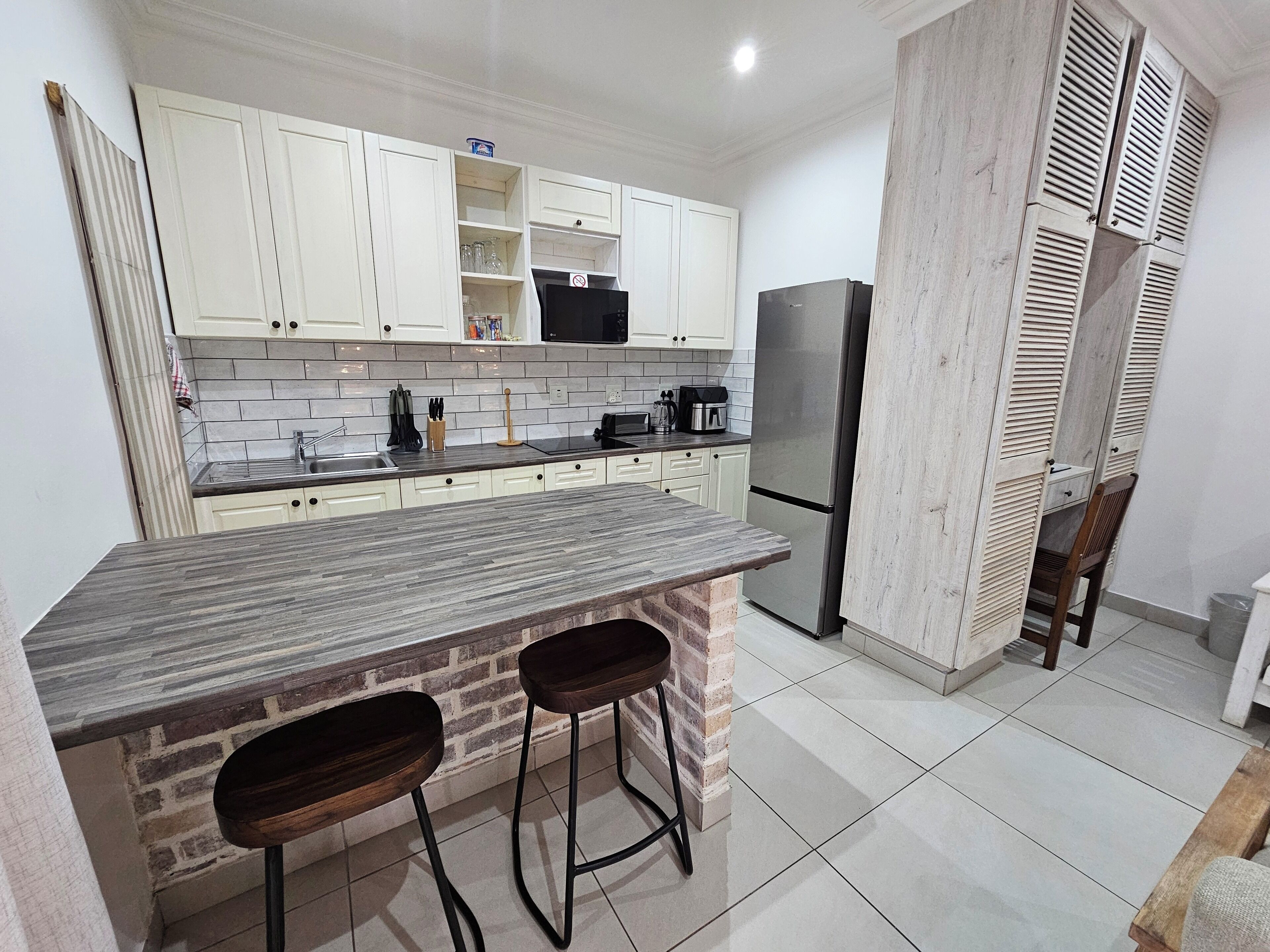 A kitchen with white cabinets, a granite countertop, a stainless steel refrigerator, and two stools.