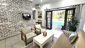 A living room with a brick wall, a TV, a pool, and a sofa. - Leopard Tree Lodge (St. Lucia)