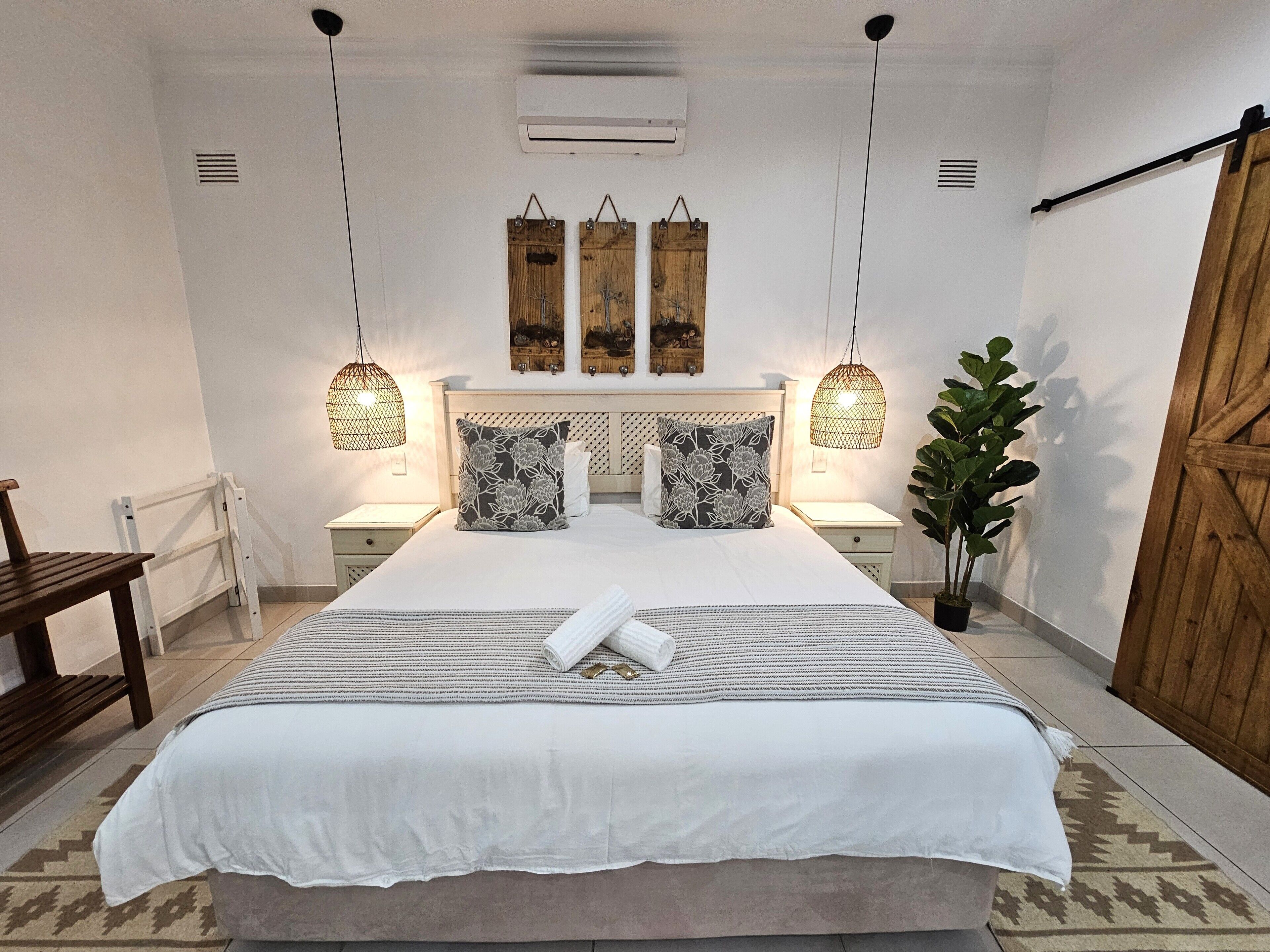 A neatly arranged bedroom with a large bed, bedside tables, hanging lights, and a potted plant.