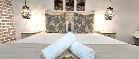 Una cama bien hecha con dos almohadas, un par de toallas enrolladas y un pequeño paquete sobre la cama.